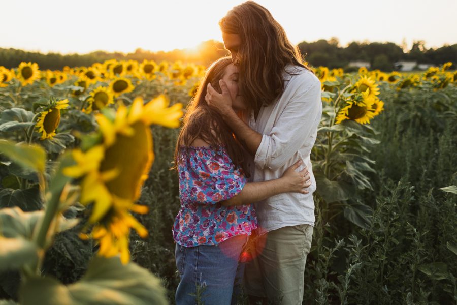 couple qui s'embrasse pendant sa séance d'engagement dans les tournesols au coucher du soleil
