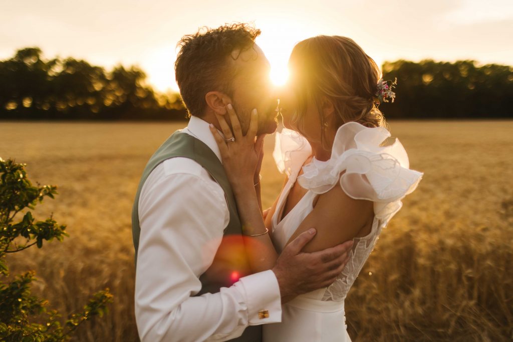 couple qui s'embrasse devant un champ de blé à la golden hour pendant leur mariage